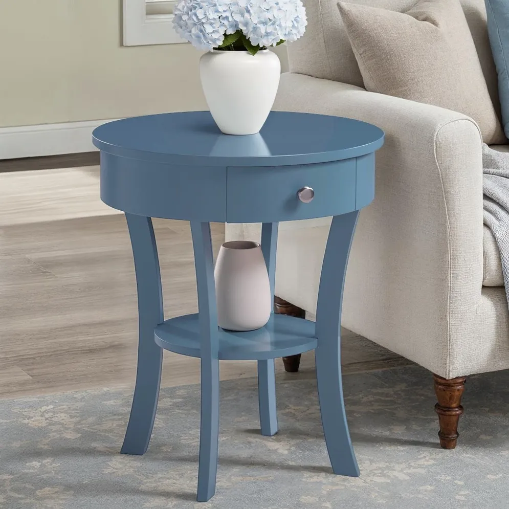 A blue round side table with a white vase holding blue hydrangeas on top, alongside a beige sofa.