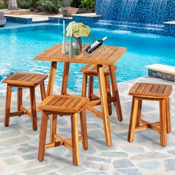 A 5-piece Acacia patio dining set with a rectangular table and four matching wooden stools, situated on a stone patio beside a pool. The table features a simple design with a bottle of wine and flowers as decoration.