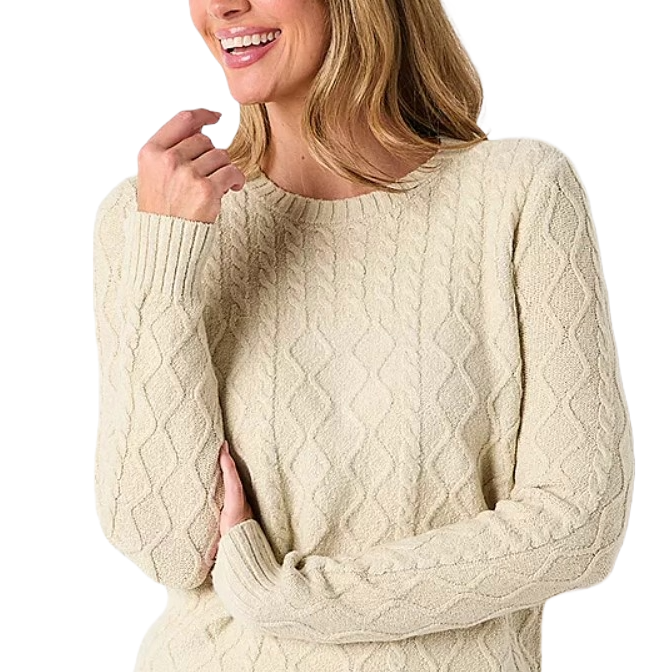 A woman wears a cream-colored, cable-knit sweater with a diamond pattern, featuring a round neckline and long ribbed cuffs.
