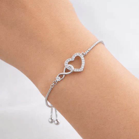 A delicate silver bracelet features an infinity symbol linked to a heart shape embellished with small clear stones, designed with an adjustable chain for a secure fit.