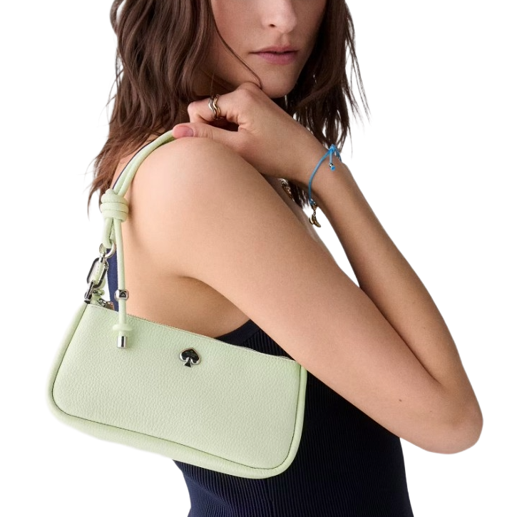 A person holds a light green shoulder bag with a spade logo, featuring a knotted strap and silver hardware.