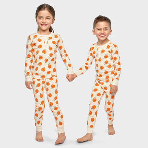 Two children are wearing matching long-sleeve pajama sets with a pumpkin pattern on a cream-colored background.