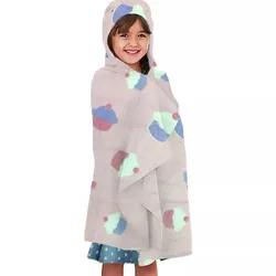 A child is wrapped in a hooded towel featuring a playful cupcake pattern in pastel colors, worn over a blue polka dot dress.