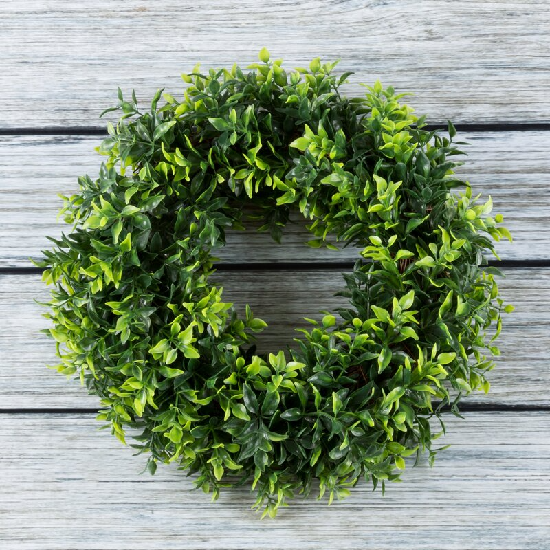 A green artificial wreath made of faux boxwood, displayed on a wooden background.