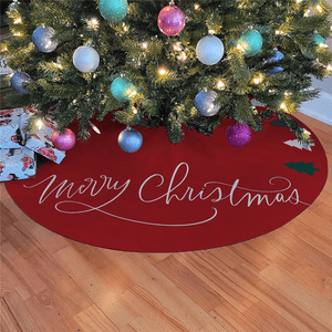 Christmas tree skirt with \“Merry Christmas\“ text, set under a decorated tree with baubles and lights. Presents with festive wrapping are placed nearby.