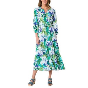 A long, floral-patterned St. John's Bay Maxi Dress in green, blue, and white features a V-neck, long sleeves, and a tiered skirt, paired with blue sandals.