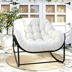 A plush white upholstered chair with a black metal frame is set on a beige circular rug outdoors, surrounded by potted orange trees in a bright, garden-like setting.