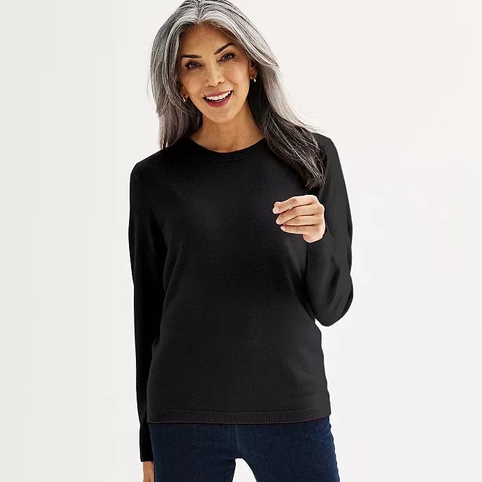 A woman is wearing a black crewneck sweater and blue jeans.