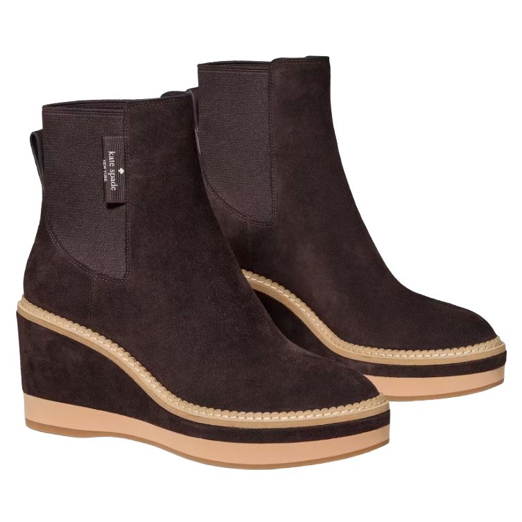 A pair of brown suede wedge ankle boots with tan soles and visible stitching. They feature elastic side panels and a pull tab for easy wear, with a label indicating they are from Kate Spade New York.