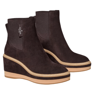 A pair of brown suede wedge ankle boots with tan soles and visible stitching. They feature elastic side panels and a pull tab for easy wear, with a label indicating they are from Kate Spade New York.