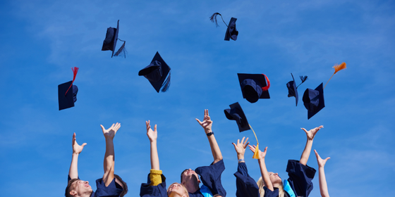 hands throwing graduation caps blue sky