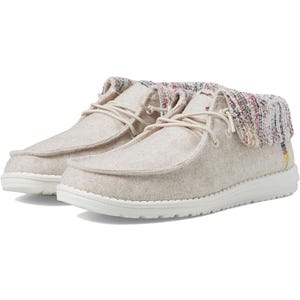 A pair of beige moccasin-style shoes with multicolored knitted detailing around the ankle.