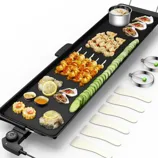 Electric griddle with various foods, including shrimp skewers, sliced cucumbers, and oysters. Accompanied by two metal rings, five spatulas, and visible controls for temperature adjustment.