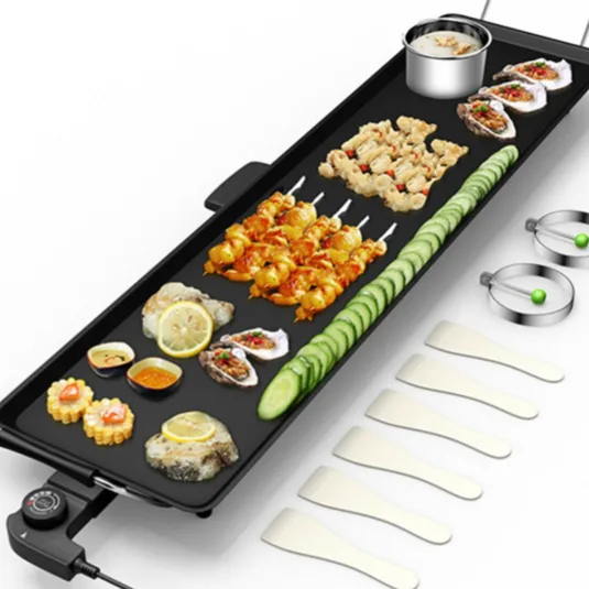Electric griddle with various foods, including shrimp skewers, sliced cucumbers, and oysters. Accompanied by two metal rings, five spatulas, and visible controls for temperature adjustment.