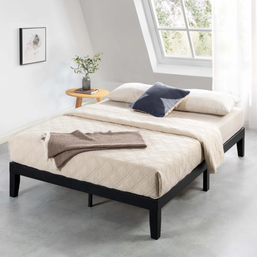 A minimalist bedroom setup features a modern bed with a black frame and beige bedding, complemented by a side table with a vase of greenery.