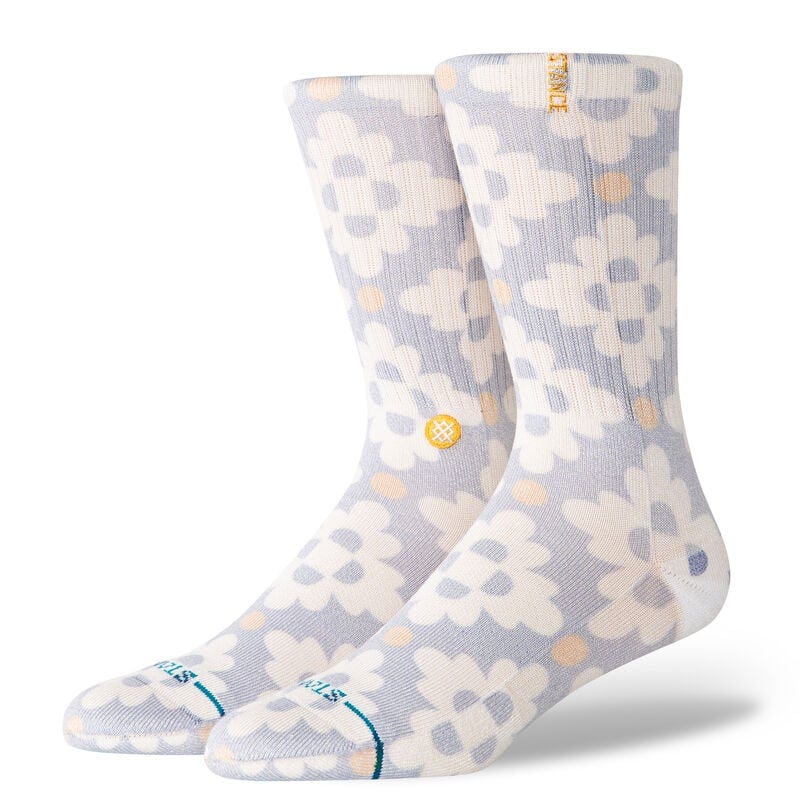Pair of light gray socks with white floral patterns and light orange dots. The cuff features the brand name \“STANCE\“ in yellow.