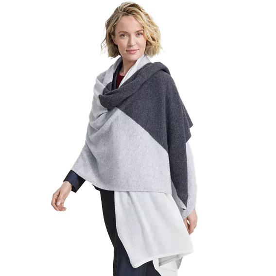 A woman is wearing a color-blocked cashmere wrap in shades of gray and white, draped over her shoulders and extending down to her waist.