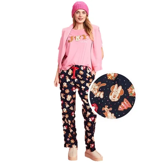 A woman wears a pink outfit featuring a top with \“Joy\“ and dark pajama pants adorned with cartoon characters. She is accessorized with a matching pink beanie and a pink sweater draped over her shoulders.