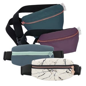 Four waist bags in teal, purple, blue, and marble pattern, each with a contrasting zipper and black adjustable strap.
