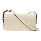 A beige leather crossbody bag by Kate Spade New York featuring a long adjustable strap and gold logo detailing on the front.
