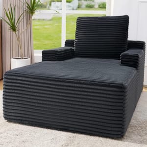 Dark gray, ribbed texture, oversized armchair with a matching back cushion, placed on a light carpet near a plant by a large window.