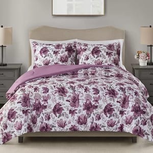 A purple floral-patterned comforter set with matching pillows on a bed, flanked by two bedside tables with lamps.