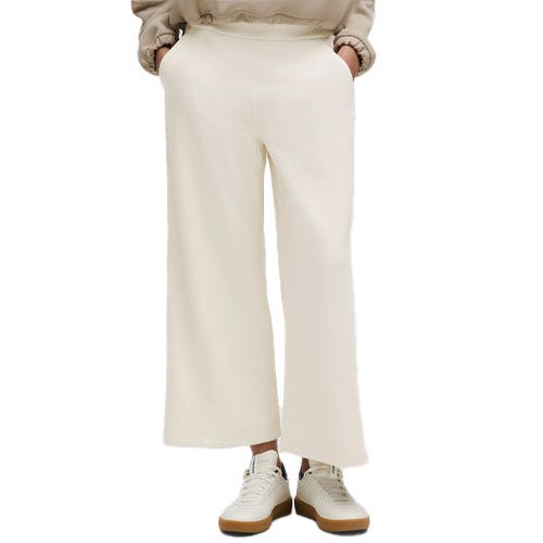 Wide-leg white pants paired with white sneakers and a beige top, with hands in pockets.
