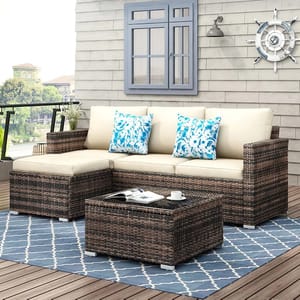 Outdoor patio set with L-shaped wicker sofa, beige cushions, blue floral pillows, and a matching coffee table. Decor includes a nautical theme with a ship's wheel and a blue patterned rug.
