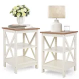 Two small side tables with a white frame and a wood top, featuring X-shaped side braces. One table holds a lamp and a glass of water, the other a vase of flowers and books.
