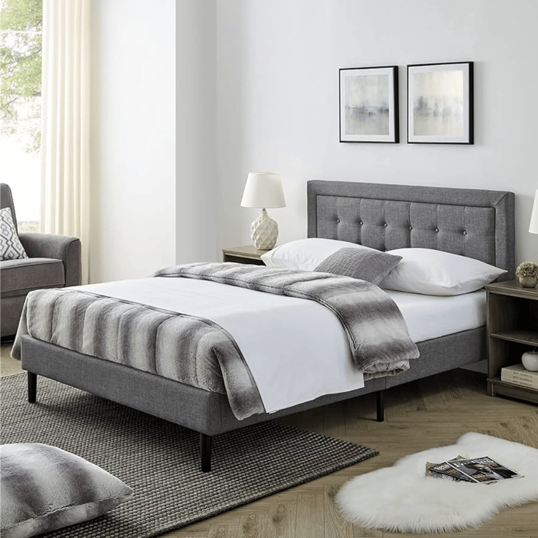 A modern bedroom features a gray upholstered bed with a button-tufted headboard, white bedding, and a striped throw. Nightstands with lamps, abstract wall art, and a cozy atmosphere complete the look.