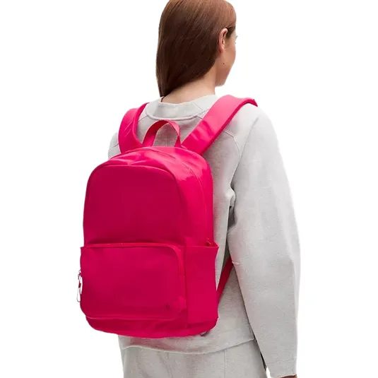 A person with long hair is wearing a vibrant pink backpack, featuring padded straps and a front pocket, paired with a light gray outfit.