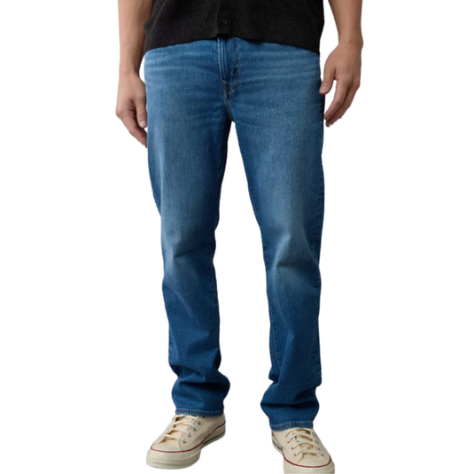 A person is wearing medium blue jeans with a slightly relaxed fit, paired with beige canvas sneakers.