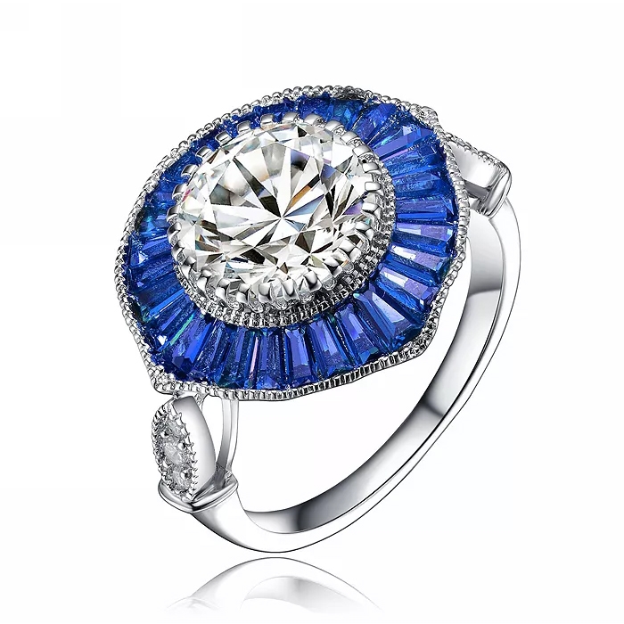 A sterling silver ring featuring a central large clear cubic zirconia stone surrounded by a halo of smaller blue baguette-cut stones, with additional small clear stones on the band.