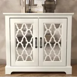 White cabinet with decorative mirrored doors, featuring a geometric pattern and black handles. Two books, an ornament, and a dark glass are placed on top.