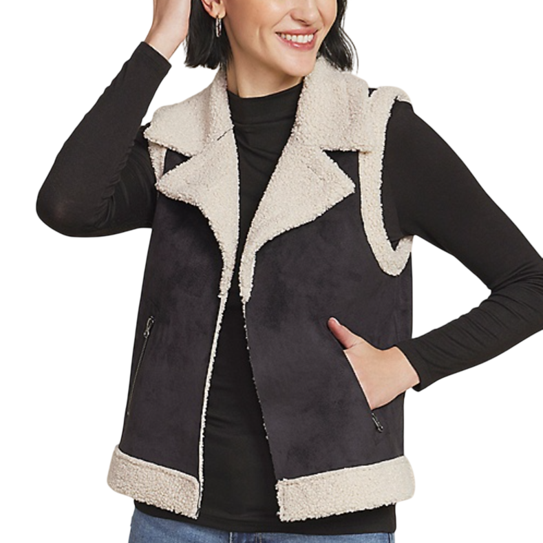 A woman is wearing a black and white sherpa-lined vest with a large collar, paired over a black long-sleeve top and light blue jeans.