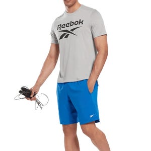 A person is holding a jump rope, wearing a gray Reebok t-shirt and blue Reebok shorts.