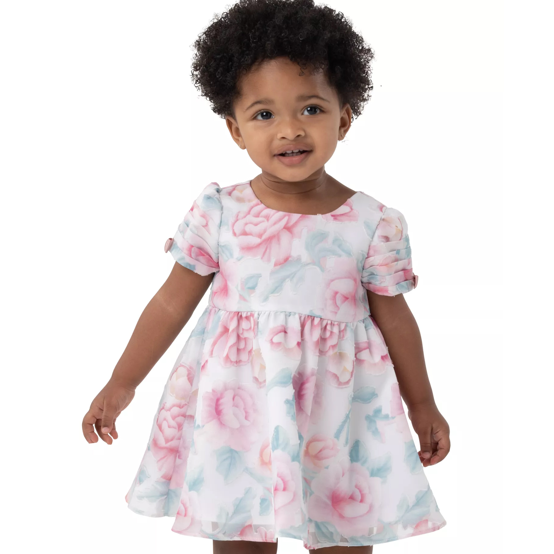 A toddler is wearing a floral dress with short puffed sleeves, featuring pink roses and green leaves on a white background.