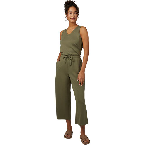 A woman is wearing a sleeveless olive green jumpsuit with a tie waist and cropped wide-leg pants, paired with flat slide sandals.