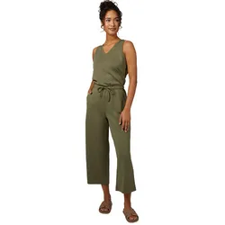 A woman is wearing a sleeveless olive green jumpsuit with a tie waist and cropped wide-leg pants, paired with flat slide sandals.