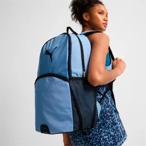 A person wearing a blue tank top is carrying a blue backpack with a visible logo and mesh side pockets.