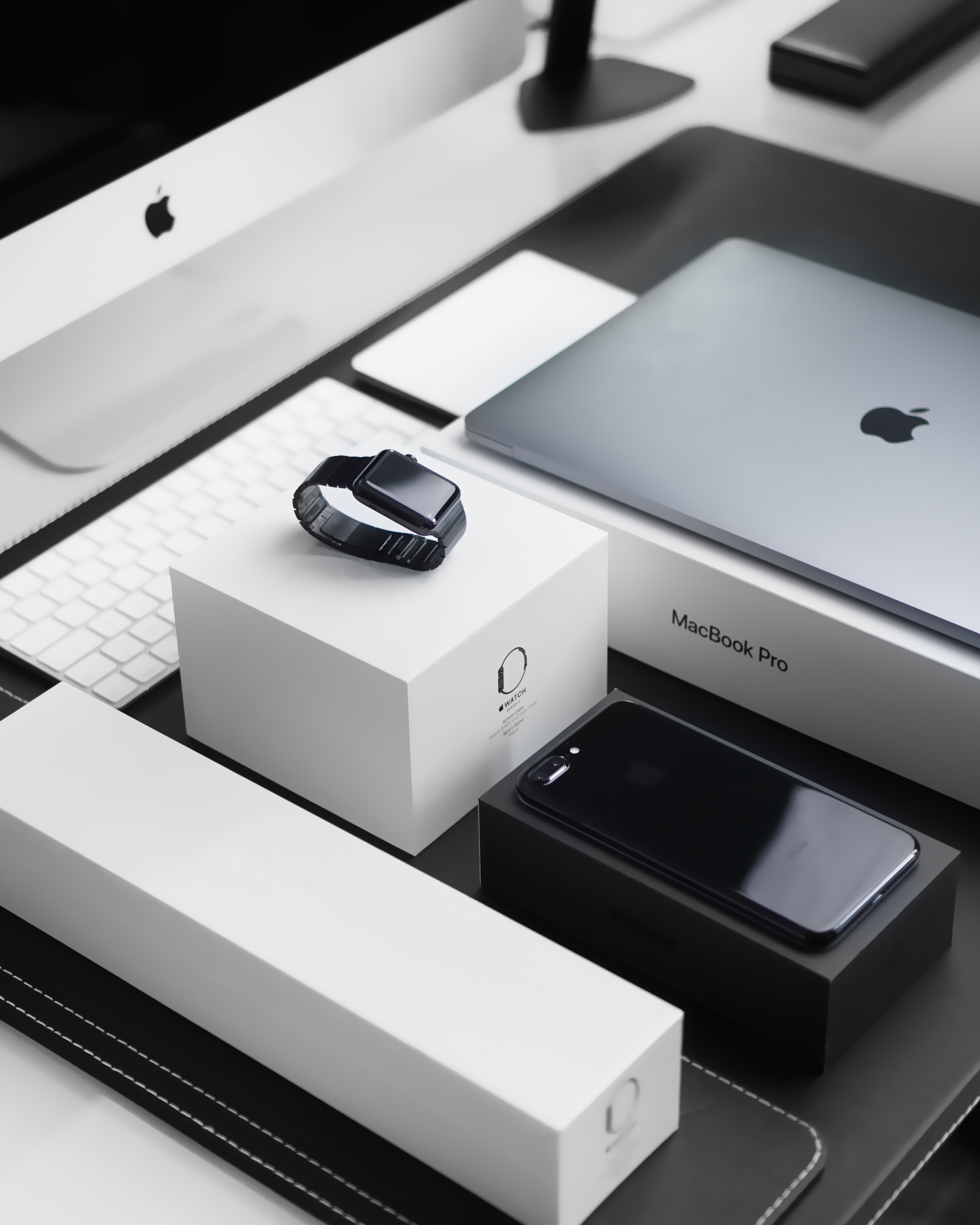 Apple devices including an iPhone, MacBook Pro, smartwatch, and accessories, arranged on a table.