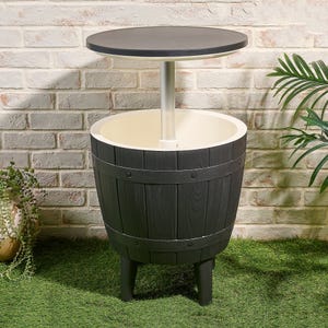 A round outdoor table with a black top and a barrel-shaped base, which also functions as an ice bucket. It stands on three legs in a garden setting, surrounded by plants and a brick wall.
