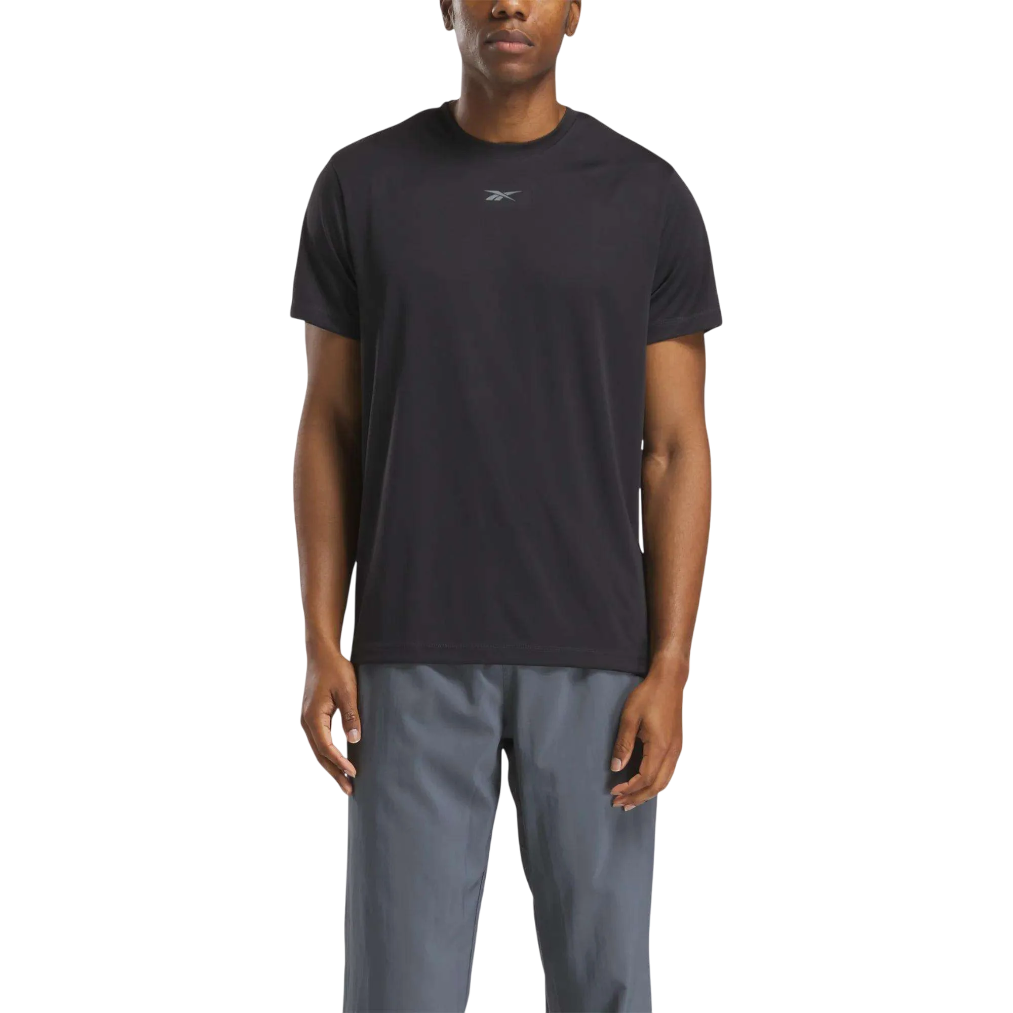 A person wearing a black Reebok t-shirt and gray pants. The t-shirt features a small Reebok logo on the chest.