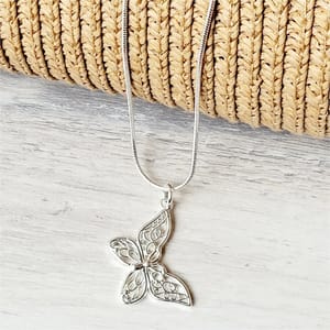 Silver butterfly pendant on a snake chain necklace, displayed on a woven textured background.