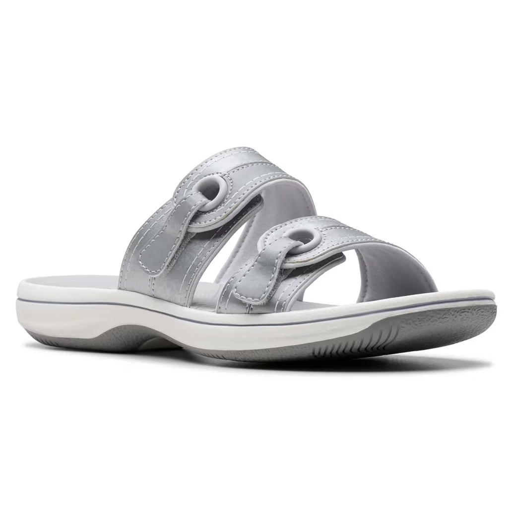 A silver slip-on sandal with two thick straps featuring circular cutout details, a slightly elevated white sole, and a textured grip bottom.
