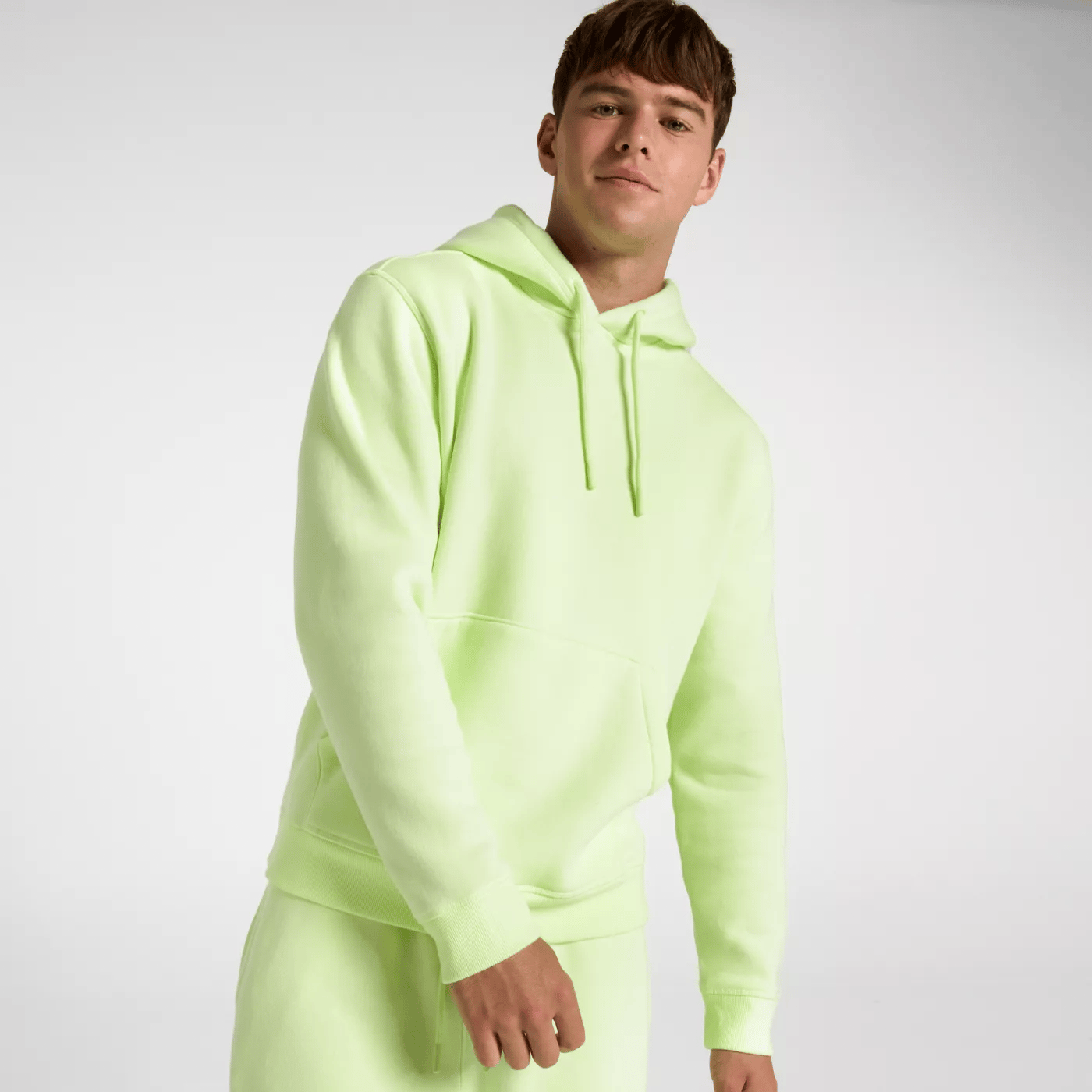 A person is wearing a bright neon yellow-green hoodie with a kangaroo pocket. The hoodie has a drawstring hood and is paired with matching jogger pants.