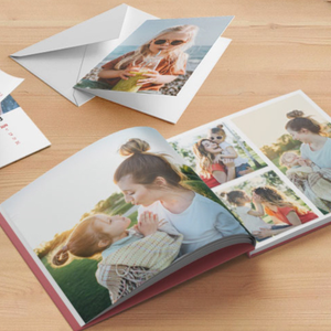 An open photo book and a card with a picture of a girl sipping a drink are displayed on a wooden surface. The book shows images of a woman and child, capturing happy moments together outdoors.