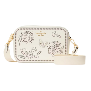 A white Kate Spade crossbody bag made from perforated leather, featuring floral and butterfly designs, gold hardware, and an adjustable strap.