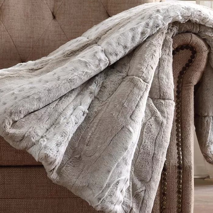 A soft, light gray faux fur throw is draped over the arm of a textured, studded beige chair.