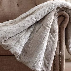 A soft, light gray faux fur throw is draped over the arm of a textured, studded beige chair.